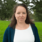 Frau mit langen, brauen Haaren, weißen Shirt und blauem Cardigan