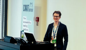 Olivia steht vor einem Rednerpult und trägt einen schwarzen Blazer